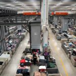 Operatori selezionano indumenti usati nell’impianto Esposito Rewear, tra contenitori e macchinari.