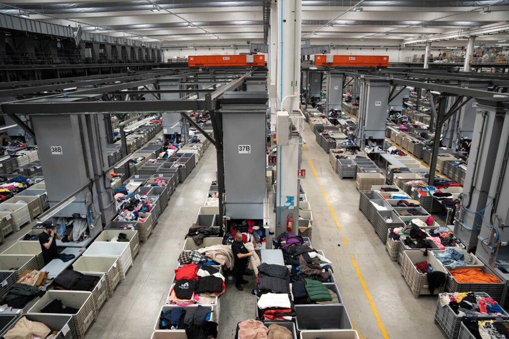 Operatori selezionano indumenti usati nell’impianto Esposito Rewear, tra contenitori e macchinari.